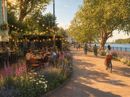 Outdoor riverside cafe with diners under string lights, bordered by colorful flowers and trees at golden hour beside a calm river.