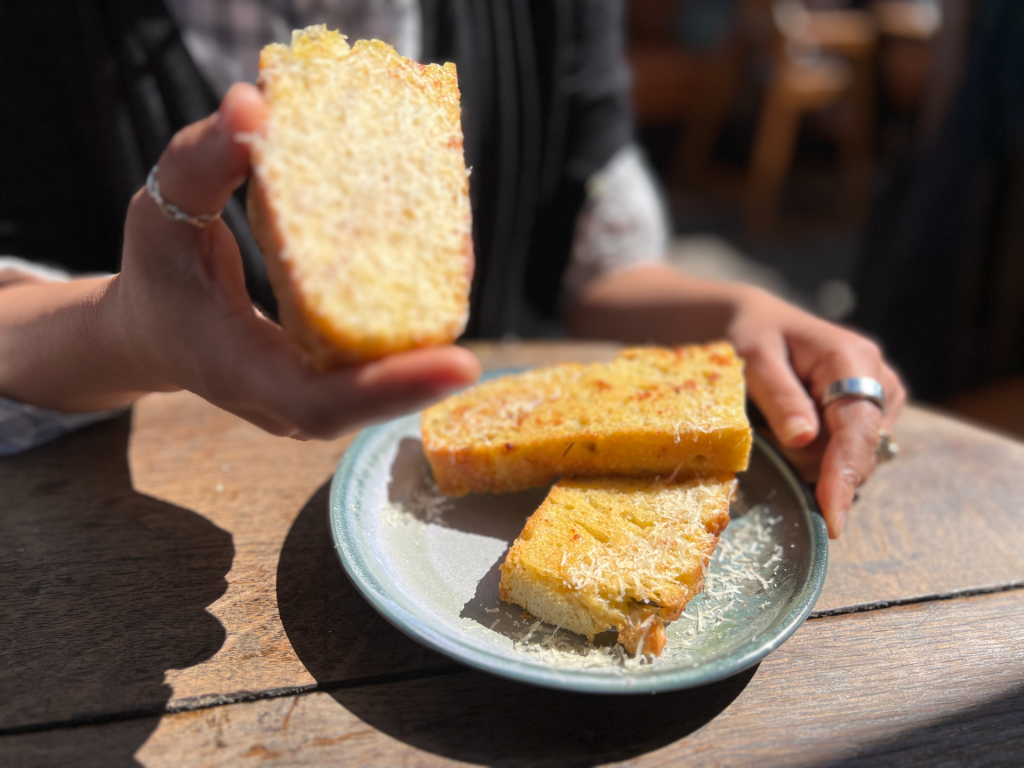 Person holding a slice of cheese cornbread over a plate of more slices on a wooden table.