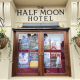 Framed wooden double doors of 'The Half Moon Hotel' with posters displayed in glass panels and two hanging planters on either side.