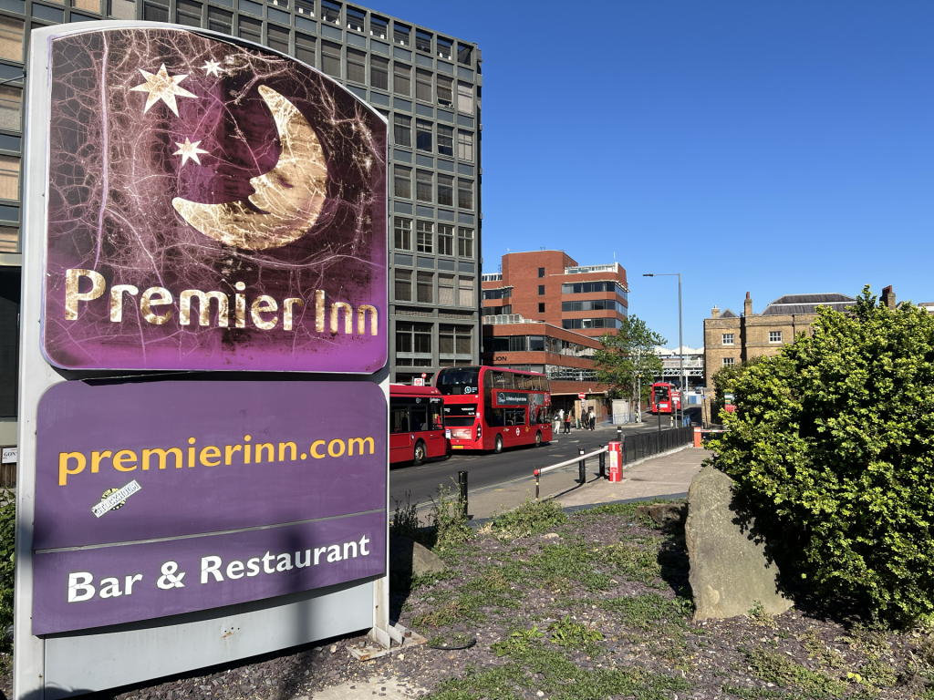Large purple Premier Inn advertisement in a city street, featuring a crescent moon and stars, with red double-decker buses and modern buildings in the background.