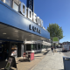 Blue Odeon Luxe cinema façade with large 3D letters along a sunny street and pedestrians nearby.