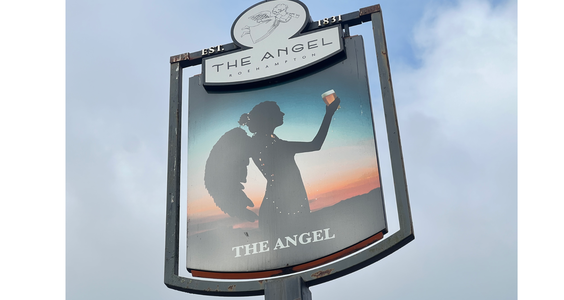 Signboard for The Angel pub showing a silhouette of a woman raising a glass against a sunset, with EST. 1831 at the top