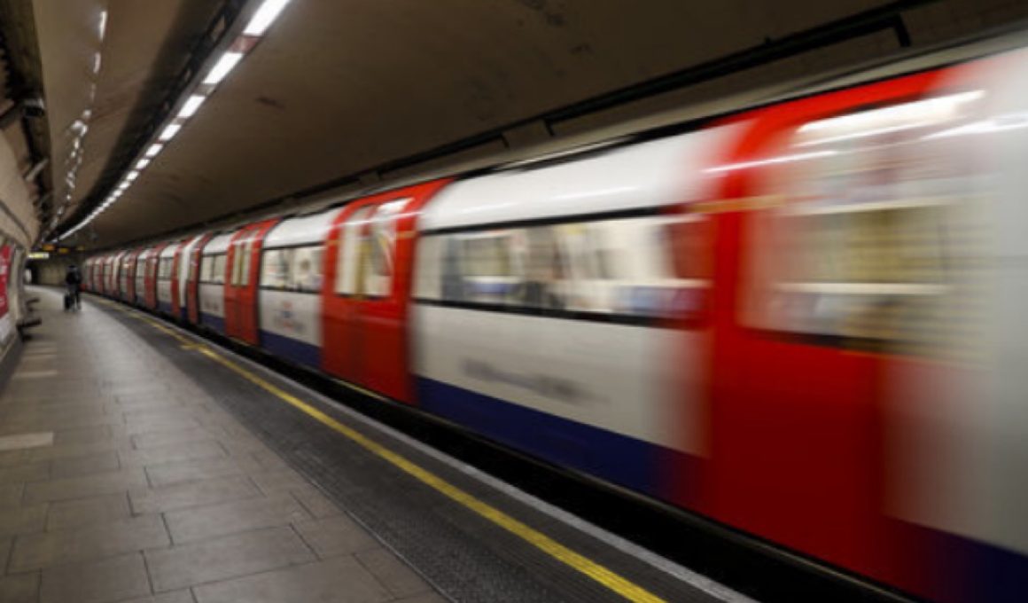 Subway train in motion at an underground platform, platform edge and tunnel visible to the left.
