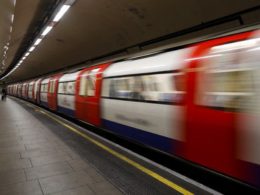 Subway train in motion at an underground platform, platform edge and tunnel visible to the left.