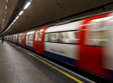 Subway train in motion at an underground platform, platform edge and tunnel visible to the left.