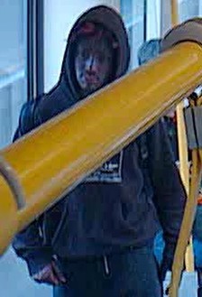 Person wearing a dark hoodie stands in a transit vehicle, partially obscured by a yellow handrail.