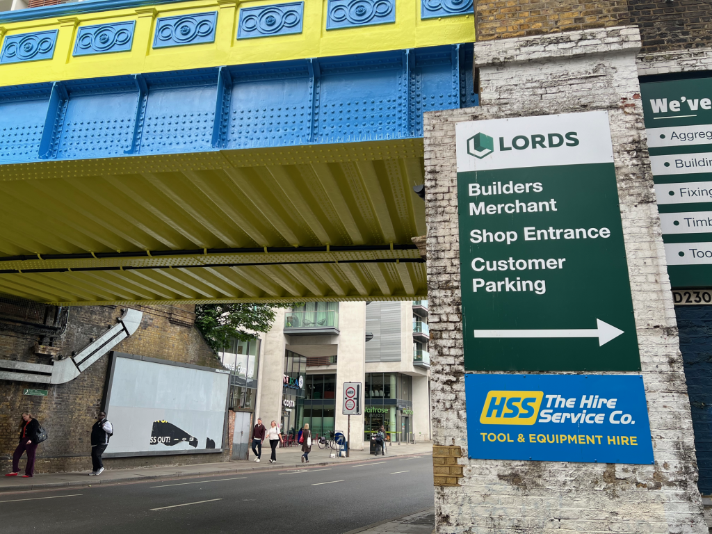 Bright yellow and blue decorative underpass over a city street, with pedestrians on the sidewalk and shopfronts below.