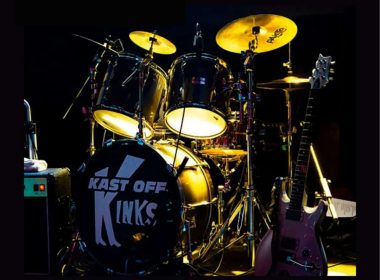 Stage drum kit setup for a band poster: black drums with 'KAST OFF KINKS' on the bass drum, yellow stage lights, and a purple electric guitar on the right; top shows band logos and a Sunday 14 June date text at the bottom.