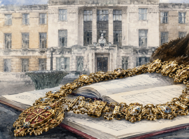 Gold ceremonial chain laid across an open book in the foreground with a grand stone building in the background.