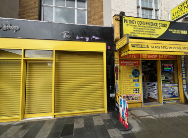 Bright yellow storefronts with closed shutters; 'Putney Convenience Store' sign and advertising boards on the right.