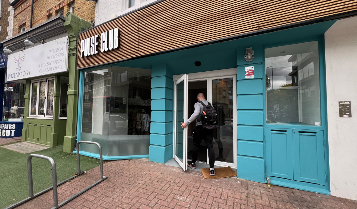 Man with backpack entering Pulse Club, a turquoise storefront on a city street.