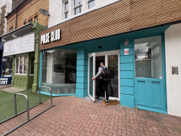 Man with backpack entering Pulse Club, a turquoise storefront on a city street.