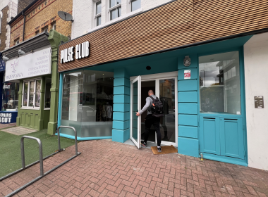 Man with backpack entering Pulse Club, a turquoise storefront on a city street.