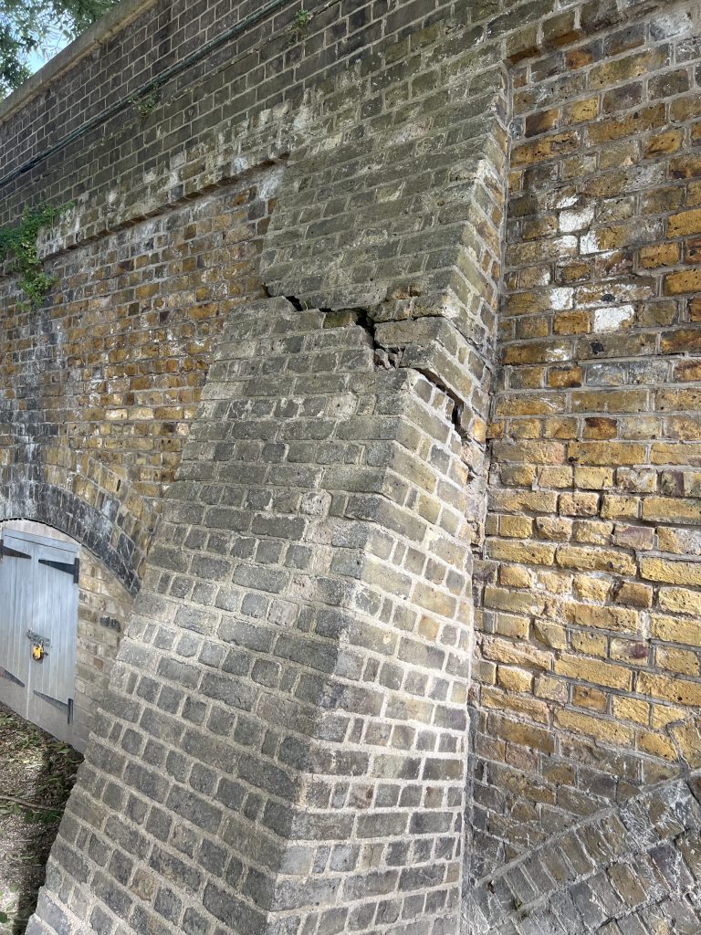 Brick wall with a stepped, weathered concrete protrusion at the corner; small door and ivy at left edge.