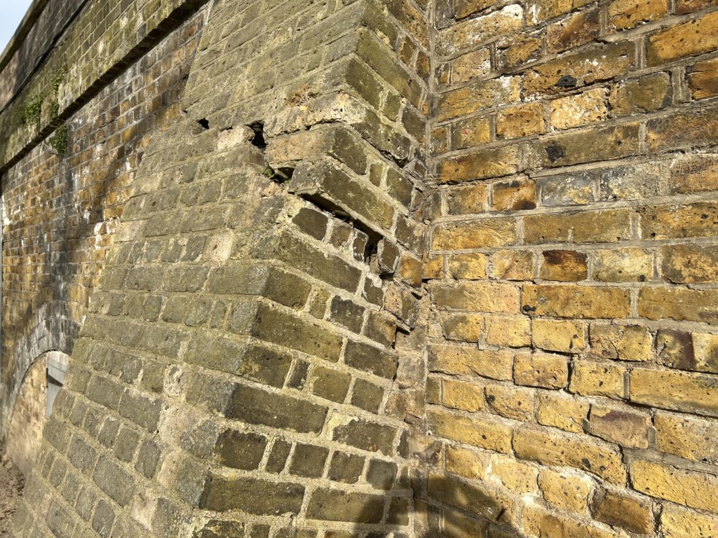 Weathered stone wall with a diagonal, stair-like stone projection and moss in the crevices.