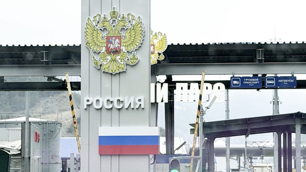 Border checkpoint entrance with large Russia emblem and the word 'РОССИЯ'; Russian flag displayed on a pillar.