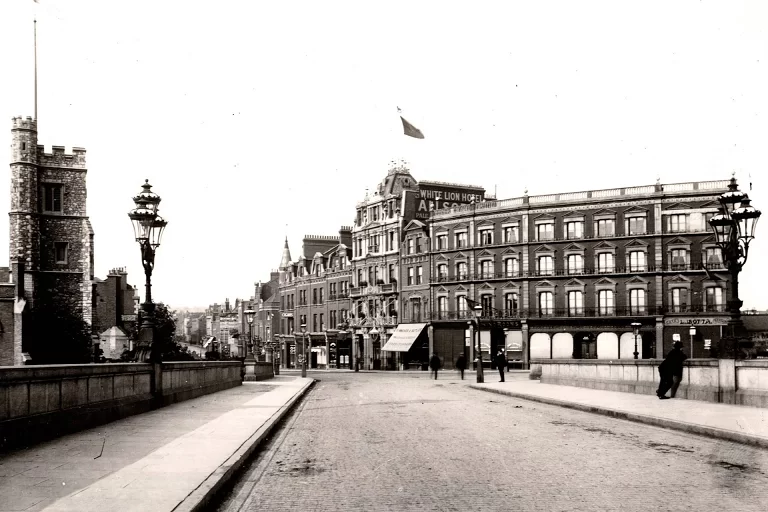 Historic street on a bridge with ornate lampposts and brick buildings along the riverfront (black-and-white).