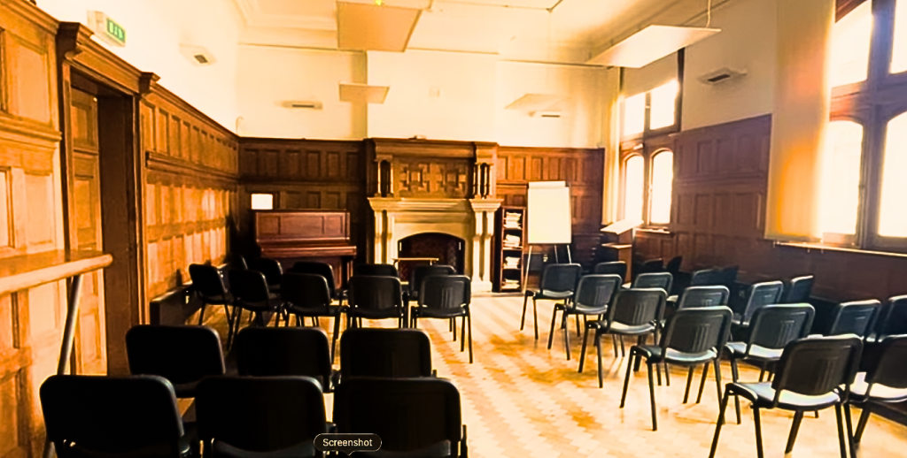 Wood-paneled meeting room with rows of black chairs facing a decorative fireplace at the front.