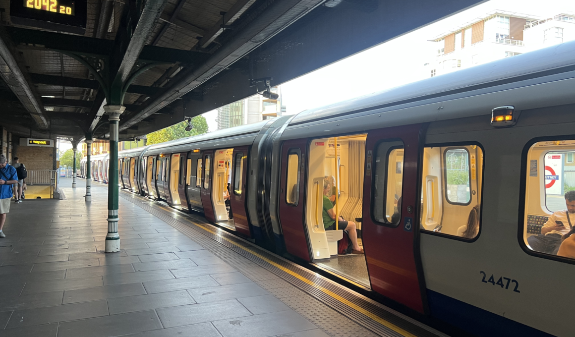 London Underground train at a platform with doors open and passengers inside, station signs visible.