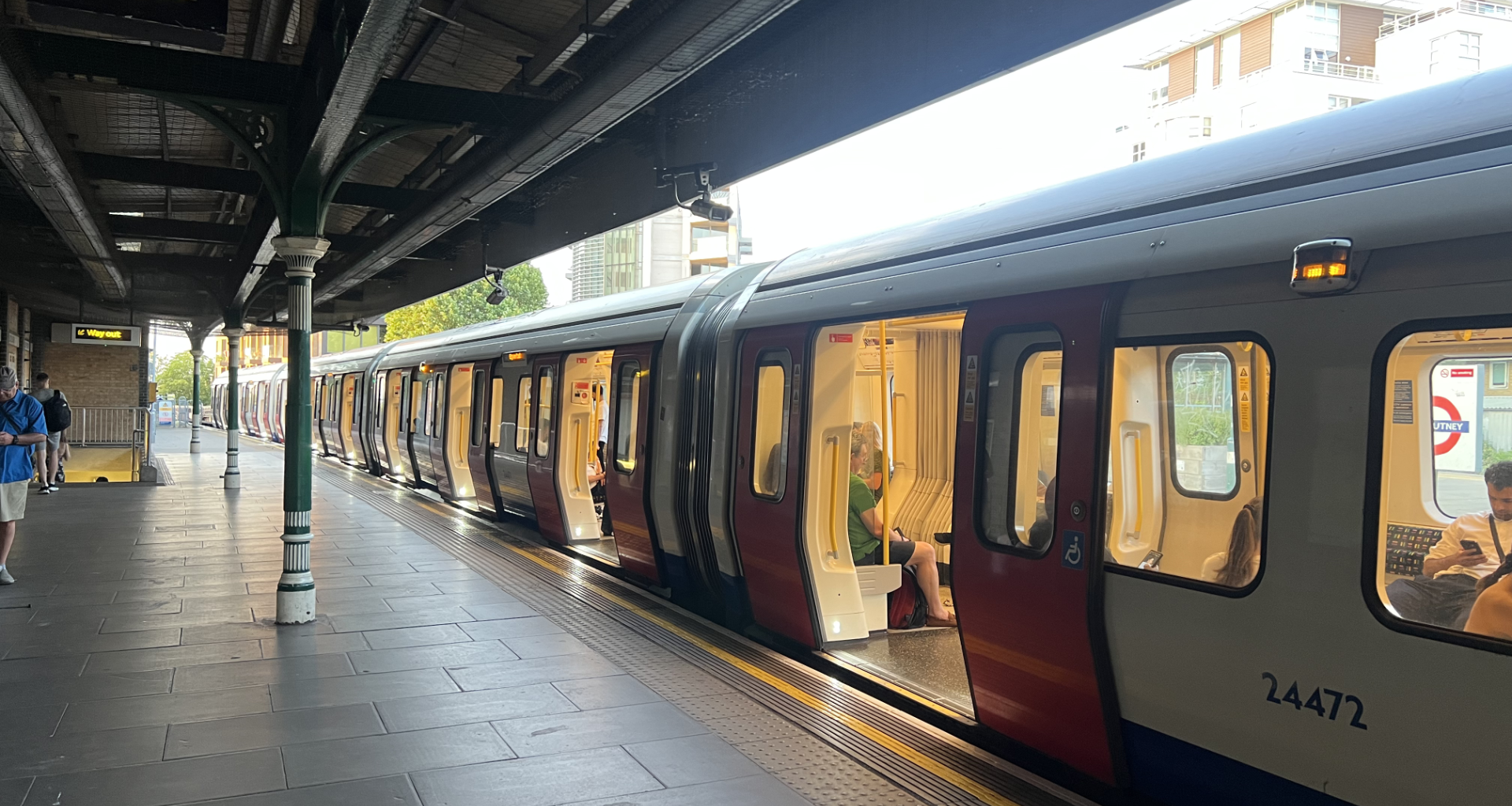 London Underground train at a platform with doors open and passengers inside, station signs visible.
