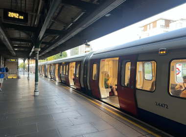 London Underground train at a platform with doors open and passengers inside, station signs visible.