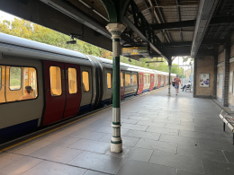 Train at a platform with a row of doors open to a warm-lit carriage; a green and white pillar stands in foreground under a metal canopy.