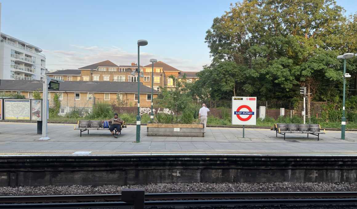 Platform at East Putney station with benches, a person sitting, and a large tree in the background