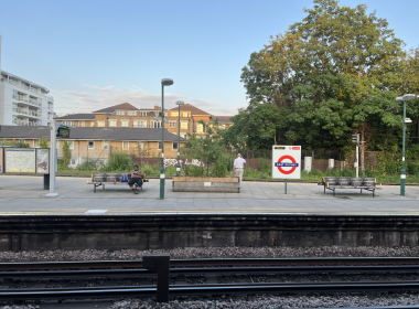 Platform at East Putney station with benches, a person sitting, and a large tree in the background
