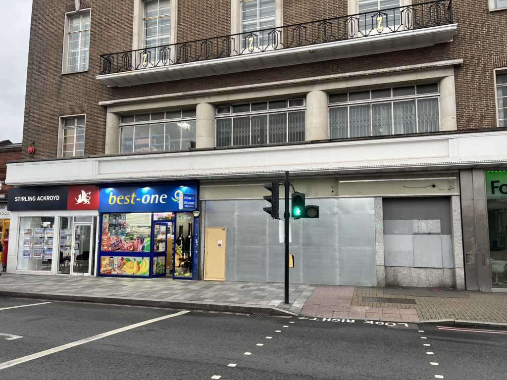 Brick building with ground-floor shops (best-one, Stirling Ackroyd) and large display windows under a white awning; brick facade above.