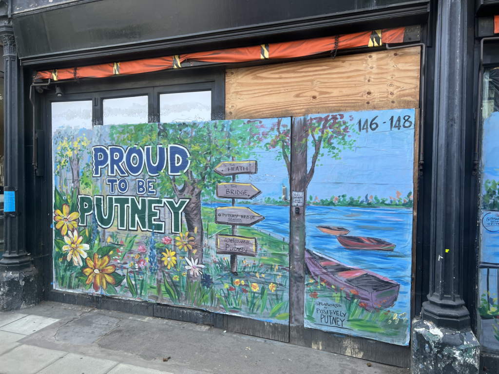 Colorful mural on a storefront: bold 'PROUD TO BE PUTNEY' with flowers, trees, and a blue sky background.