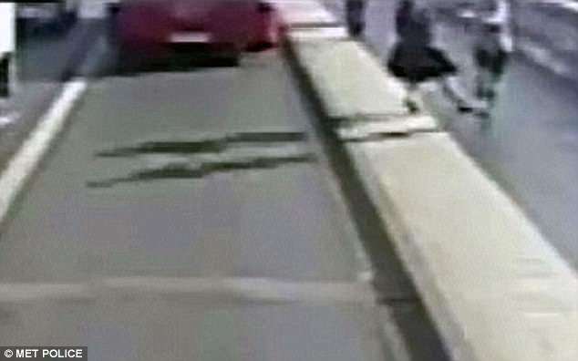 Blurry street scene showing a sidewalk with a low barrier, a parked red car in the distance, and a person walking nearby.