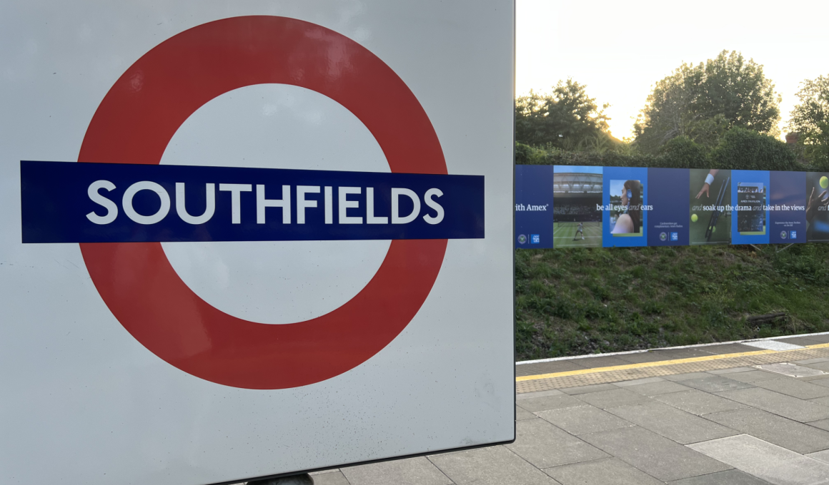 Close-up of a white sign with a red circle symbol and bold blue 'SOUTHFIELDS' text, platform edge visible to the right.