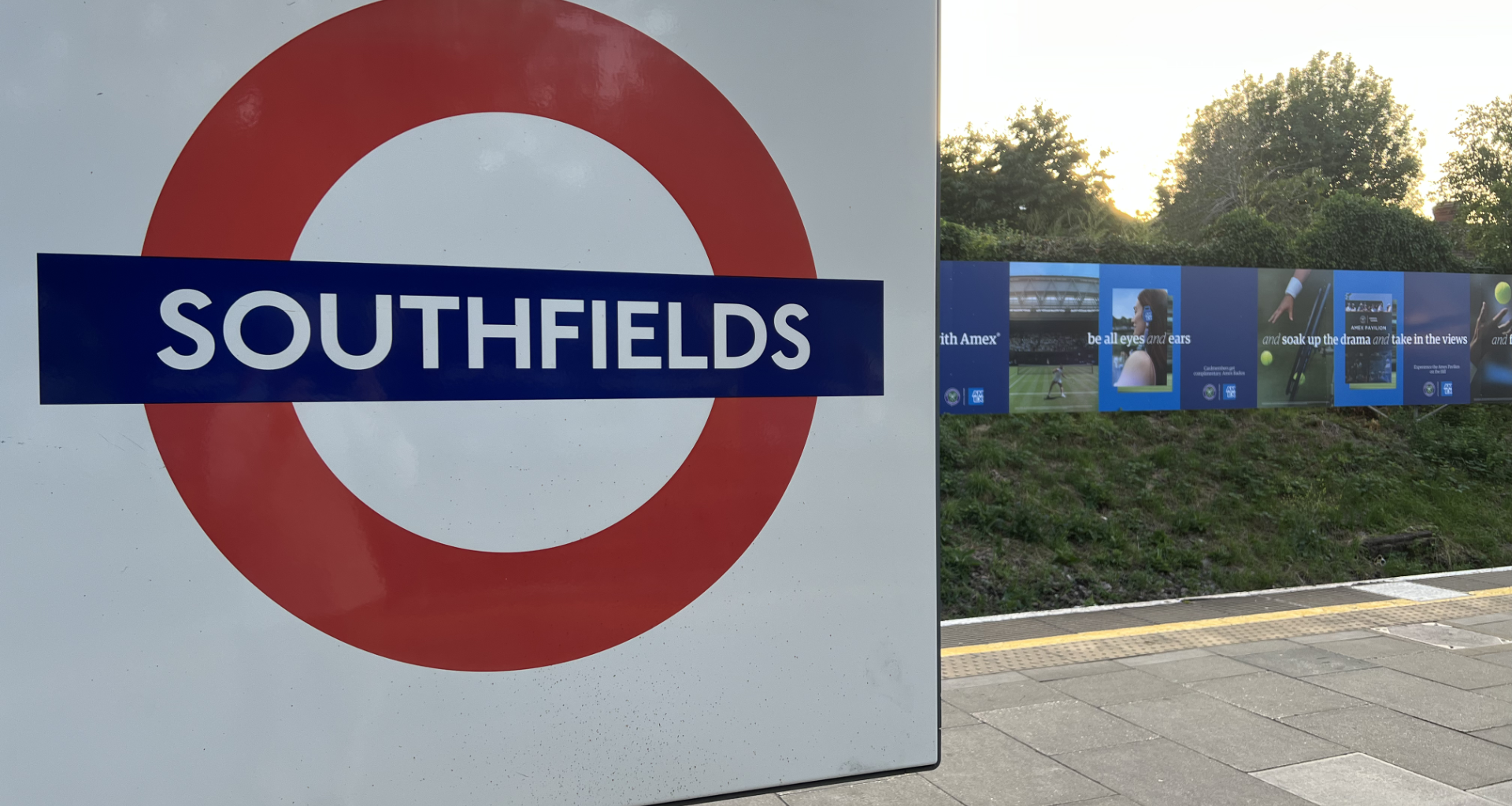 Close-up of a white sign with a red circle symbol and bold blue 'SOUTHFIELDS' text, platform edge visible to the right.