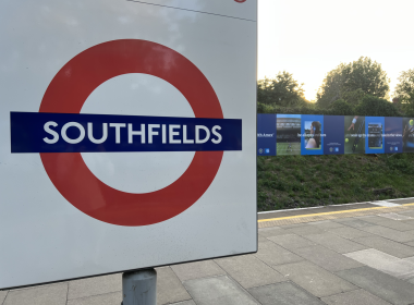 Close-up of a white sign with a red circle symbol and bold blue 'SOUTHFIELDS' text, platform edge visible to the right.