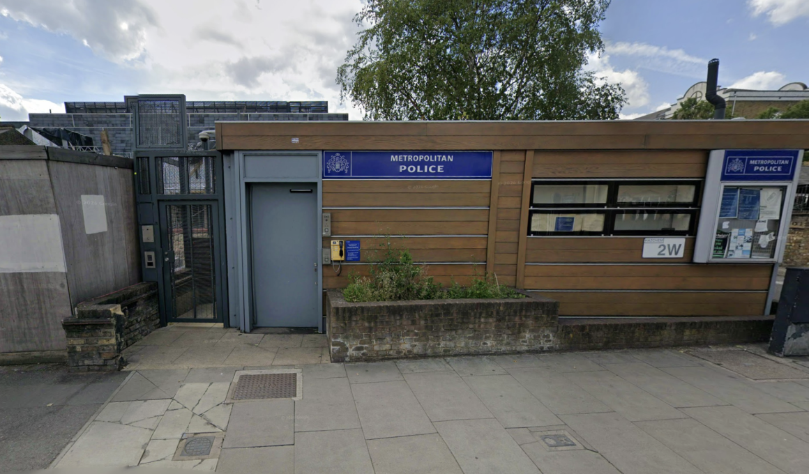Exterior view of a Metropolitan Police outpost with a blue sign, wooden panel facade, and bulletin board windows on a city street.