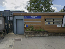 Exterior view of a Metropolitan Police outpost with a blue sign, wooden panel facade, and bulletin board windows on a city street.