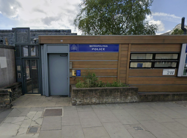 Exterior view of a Metropolitan Police outpost with a blue sign, wooden panel facade, and bulletin board windows on a city street.