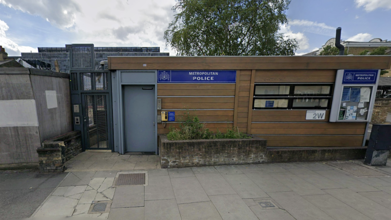 Exterior view of a Metropolitan Police outpost with a blue sign, wooden panel facade, and bulletin board windows on a city street.