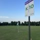 Tall sign on a pole in a grassy field reading 'Queue Section' with large 'K' and '10' and arrows 'A' and 'B' for directions below left and right.