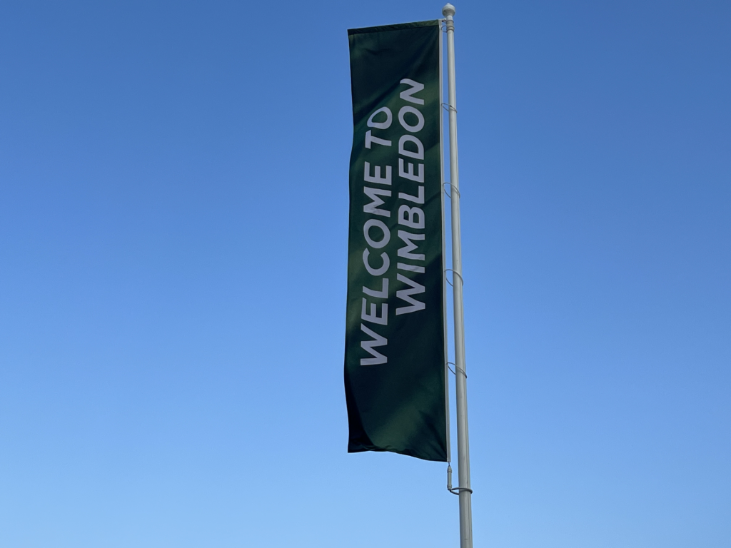 Tall green vertical banner on a flagpole with white vertical text reading 'WELCOME TO NEW ZEALAND' against a clear blue sky.