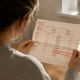 Woman at a kitchen table reading a payslip with a line marked ‘DEDUCTION’ highlighted in red