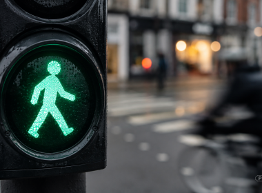 Green pedestrian crossing signal as a cyclist speeds through the wet high street behind it.
