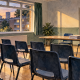 Watercolour illustration of an empty community clubroom on a London council estate, with rows of plastic chairs facing a trestle table stacked with meeting papers and post-war housing visible through the windows at sunset.