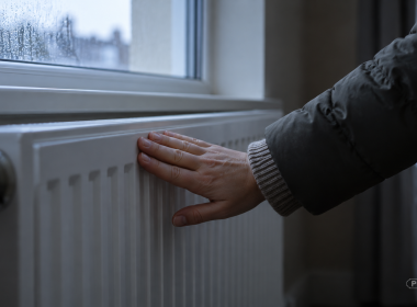 A hand in a coat sleeve pressed against a radiator, testing it for warmth