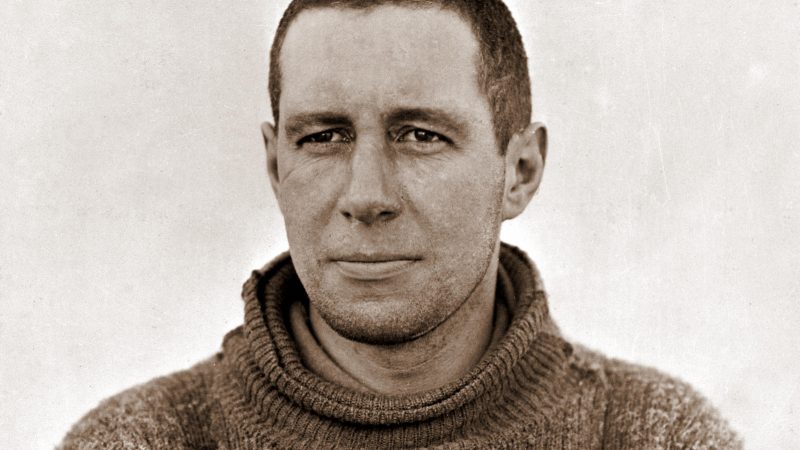 Black and white portrait of Lawrence Oates, head and shoulders, in a thick roll-neck jumper, looking straight at the camera.