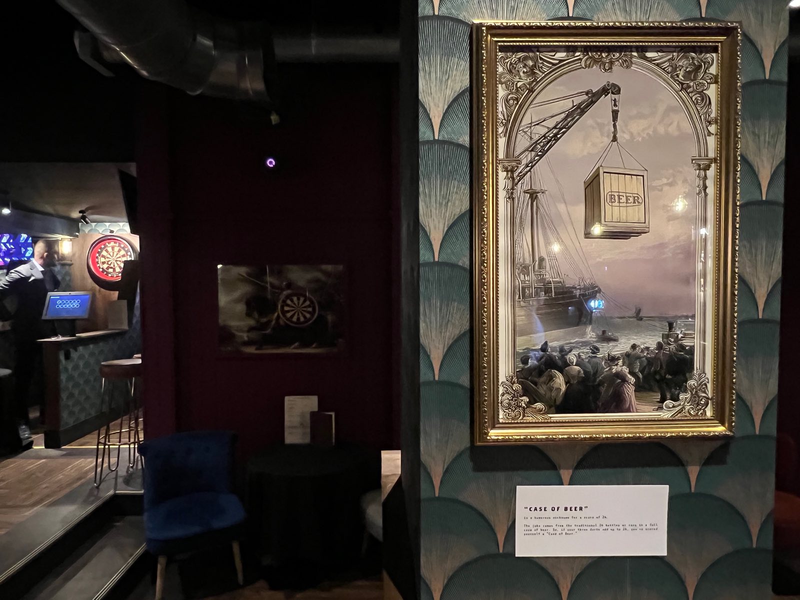 A framed painting of a crate of beer hanging from a crane, captioned Case of Beer