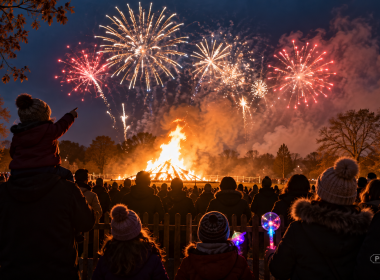 Families watch a Bonfire Night celebration in a park, with a large bonfire blazing beneath colourful fireworks.