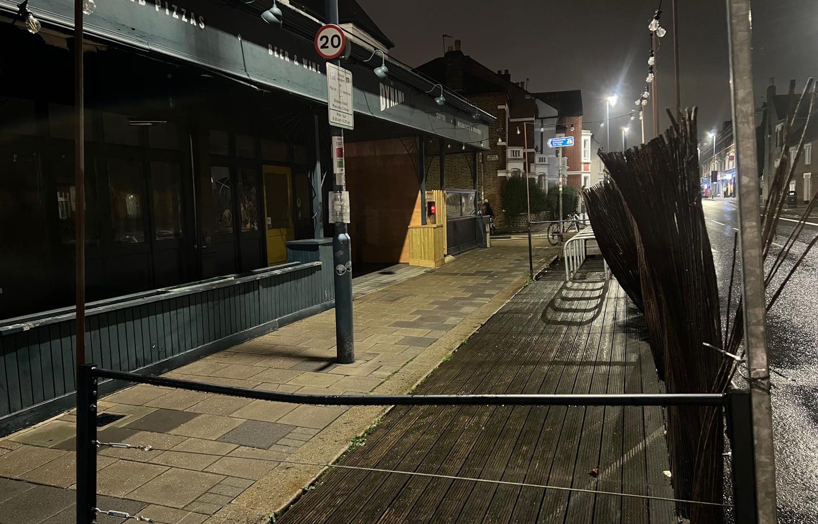 The closed Dynamo on Putney Bridge Road at night, its wooden terrace running along the kerb in front of it, with cycle stands on the decking and a new timber hoarding over the unit next door