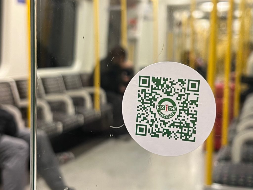 A Fix the District QR code sticker on a glass panel inside a District line train