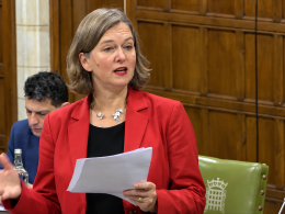 Fleur Anderson, in a red jacket, speaks from notes in Westminster Hall, with another MP seated behind her